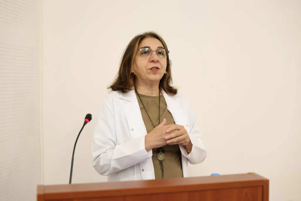 Kürsüde konuşan beyaz önlüklü bir öğretim üyesi