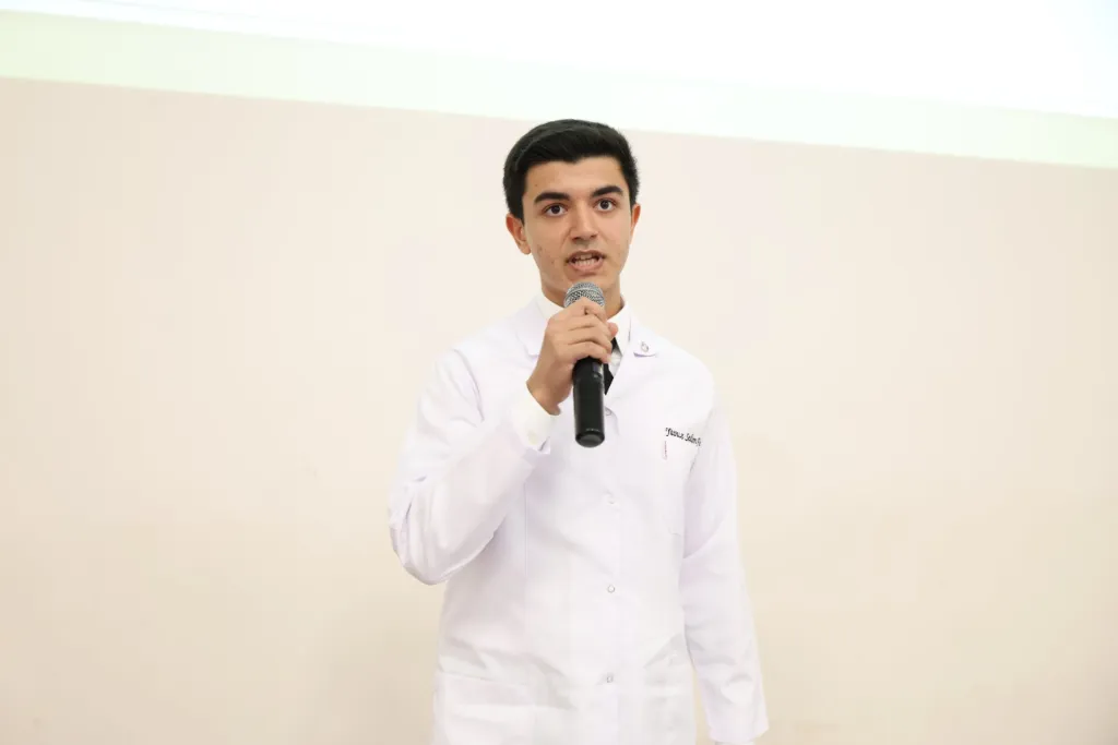 Elinde mikrofonla şiir okuyan beyaz önlüklü öğrenci