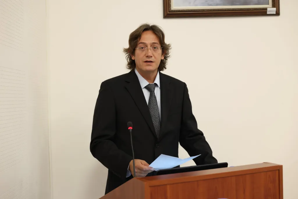 Kürsüde elindeki metinden konuşma yapan bir öğretim üyesi
