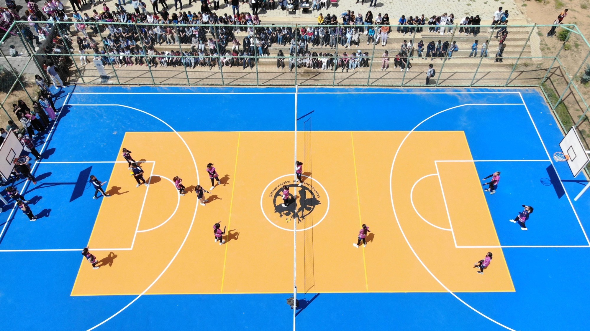 Children and the school community gathering around the new volleyball court